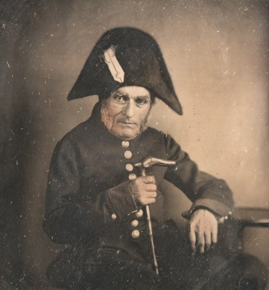 Pensionnaire de l'Hôtel des Invalides en uniforme, assis, accoudé à un guéridon. Photographie de 1850