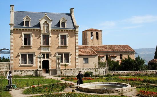 La Villa Béthanie de l'abbé Saunière, avec son potager, à Rennes-le-Châeau (Aude). Béranger Saunière pose devant le bassin circulaire. À droite, l'église. Carte postale d'époque, colorisée ultérieurement